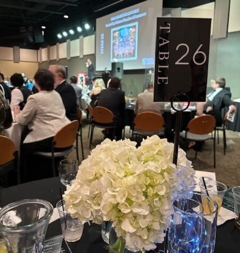 A group of people sitting at tables with vases and flowers.