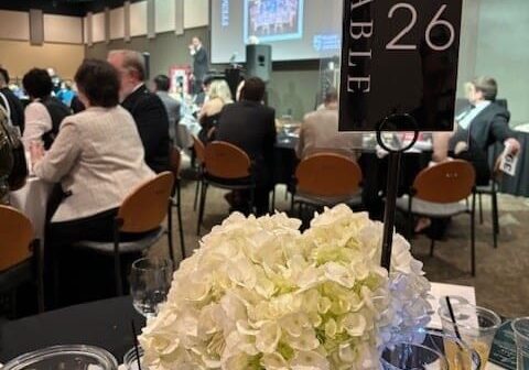 A group of people sitting at tables with vases and flowers.